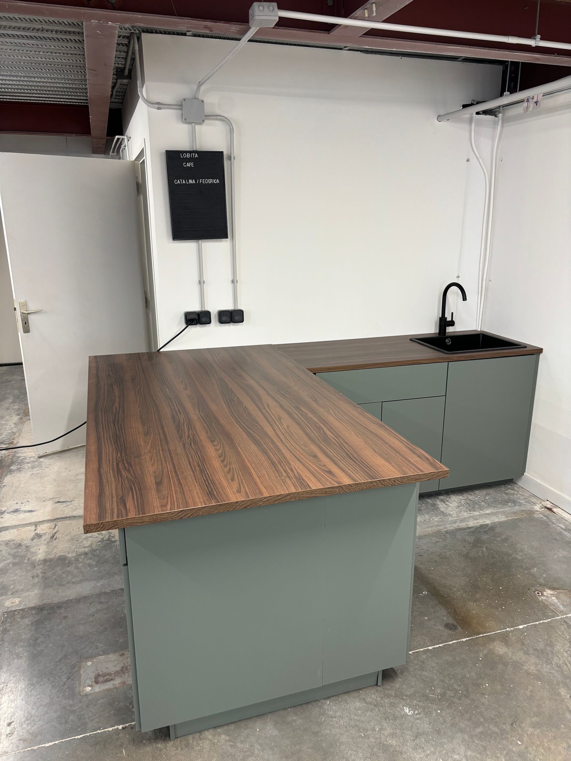 Petit coin cuisine moderne avec îlot central en bois, placards gris, évier noir et murs blancs.