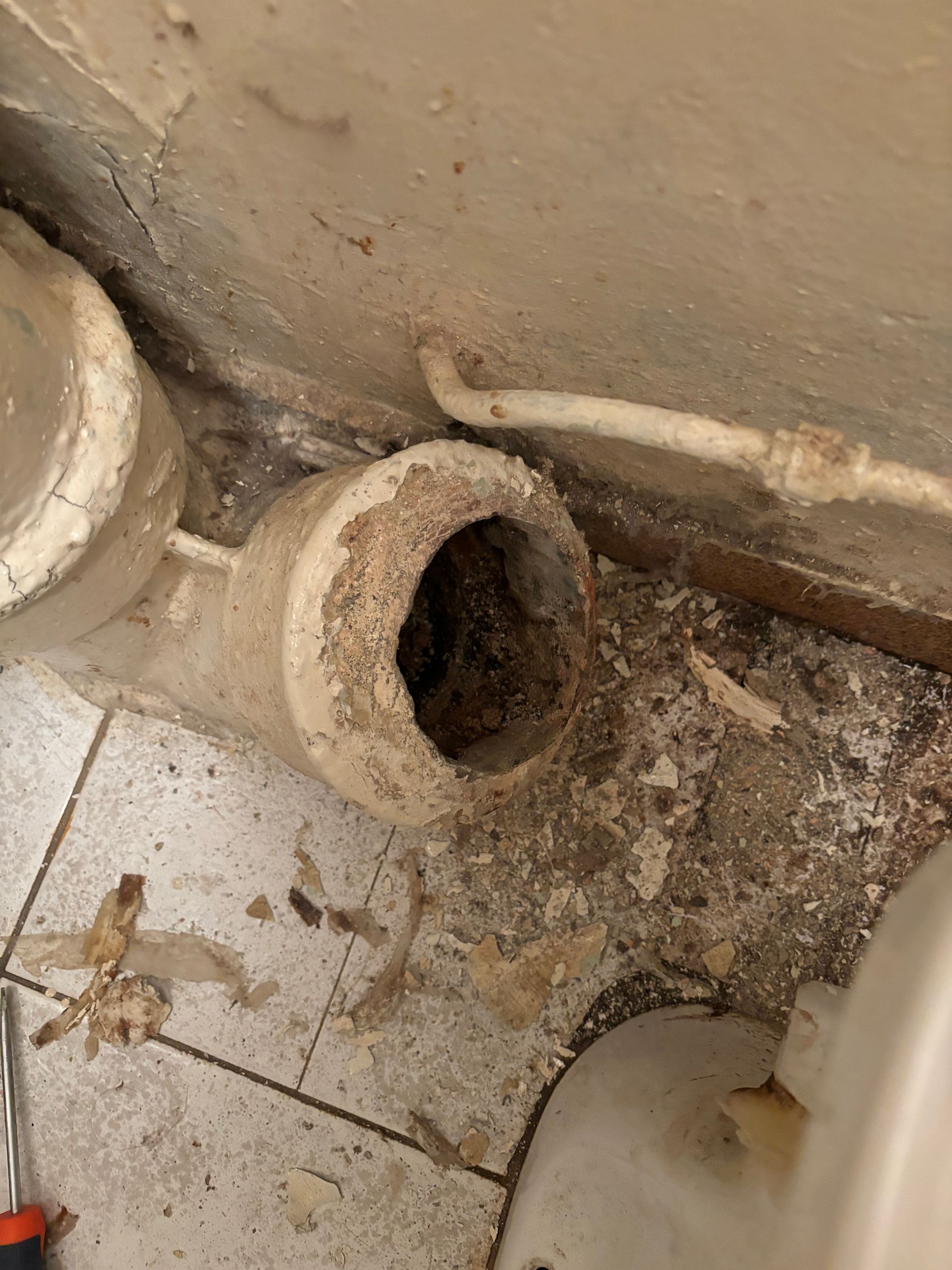 Sol de salle de bains sale, tuyau d'évacuation cassé et débris autour de l'ouverture.