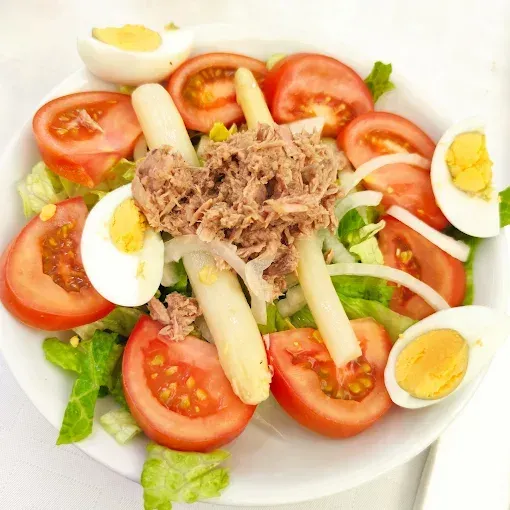 Ensalada en plato blanco: tomates, huevos duros, espárragos blancos, atún, cebolla y lechuga.