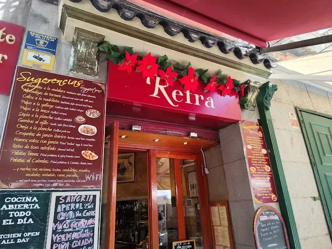 Entrada al restaurante Retra, cartel rojo con guirnalda de flores, puerta abierta, tablero de menú.