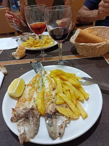 Pescado a la plancha con patatas fritas y limón, servido con vino y pan.