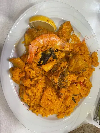 Paella con camarones, mariscos y rodaja de limón en un plato blanco.
