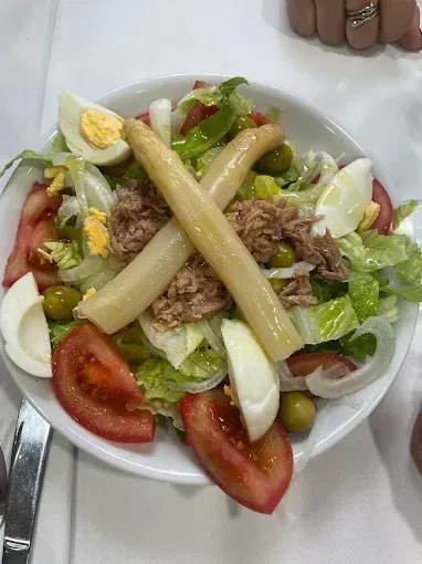 Ensalada con tomates, huevos, espárragos, atún y aceitunas en un bol blanco.