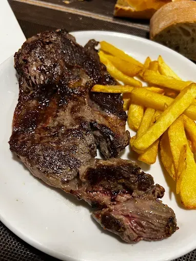 Filete a la parrilla y patatas fritas en un plato blanco. Pan francés de fondo.