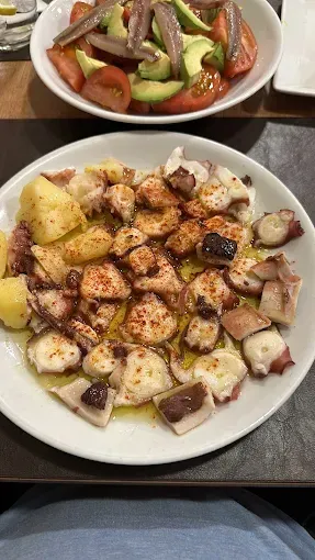 Plato de pulpo a la gallega con patatas, espolvoreado con pimentón. Ensalada de tomate, aguacate y anchoas.