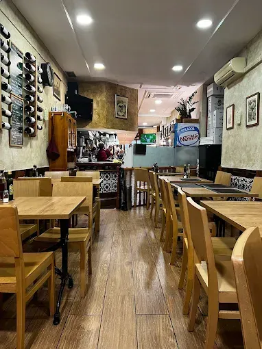 Interior de un restaurante con mesas y sillas de madera. Botellero en la pared izquierda.