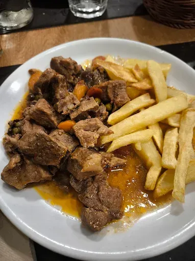 Carne y verduras guisadas con patatas fritas en un plato blanco.