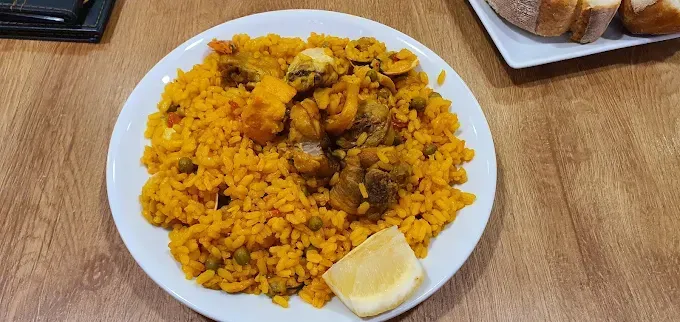 Un plato de paella con camarones, mejillones y una rodaja de limón.