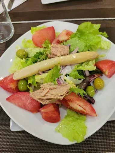 Ensalada con tomates, atún, espárragos, aceitunas y lechuga en un plato blanco.