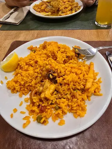Paella con gajo de limón en un plato, junto a un plato de pasta en una mesa.