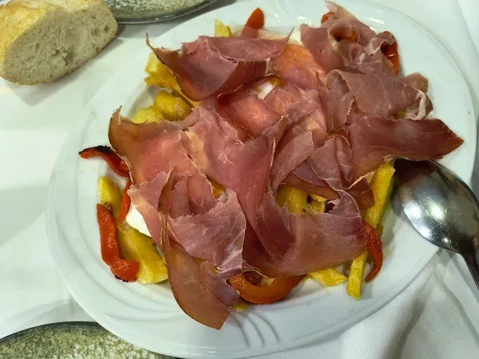 Plato de patatas fritas, pimientos rojos y prosciutto.