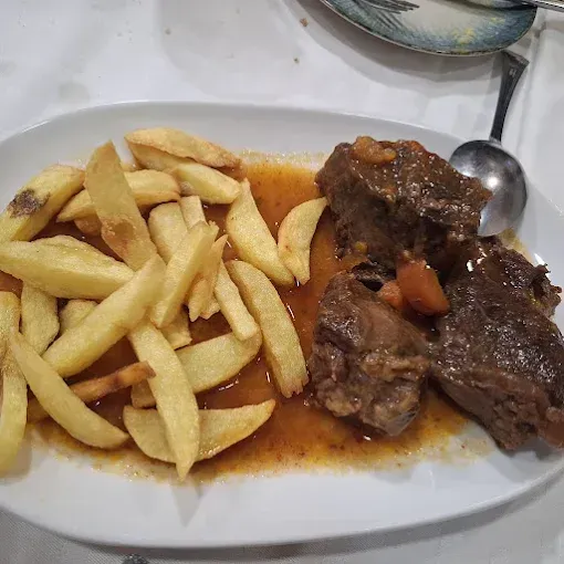 Plato de estofado de ternera con patatas fritas. El estofado lleva salsa marrón.