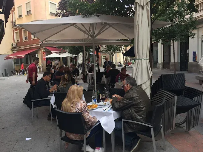 Restaurante al aire libre con gente sentada en mesas bajo una gran sombrilla.