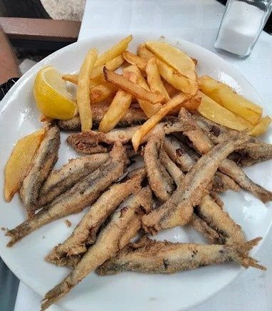 Pescado frito y patatas fritas en un plato blanco con una rodaja de limón y un salero en el fondo.