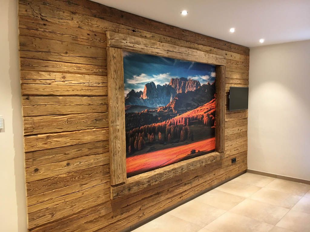 An einer Holzwand hängt ein Bild einer Berglandschaft.