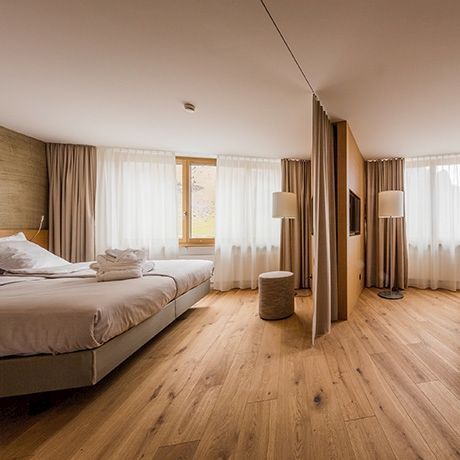 Ein Hotelzimmer mit zwei Betten, Holzboden, Vorhängen und einem Fernseher.