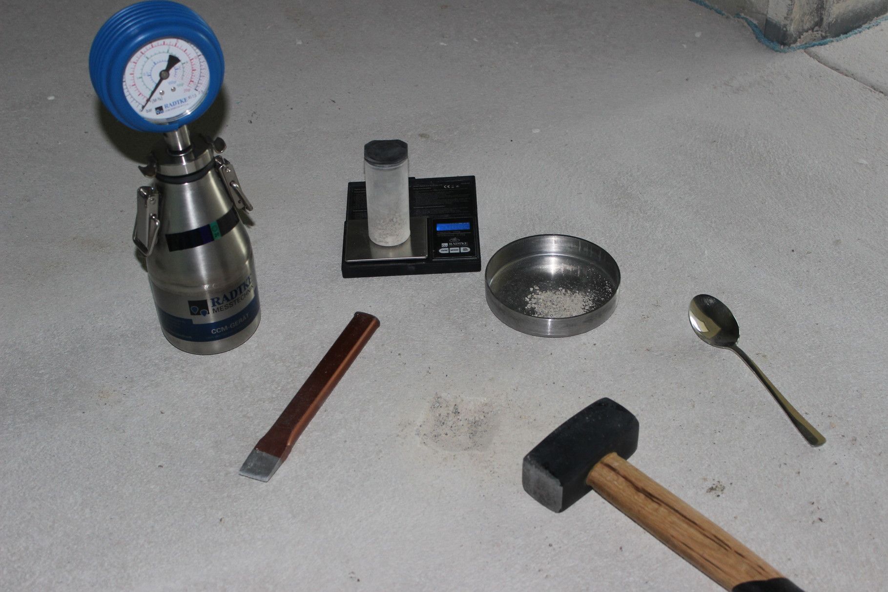 Ein Hammer, ein Löffel, eine Waage und ein Druckmesser liegen auf dem Boden