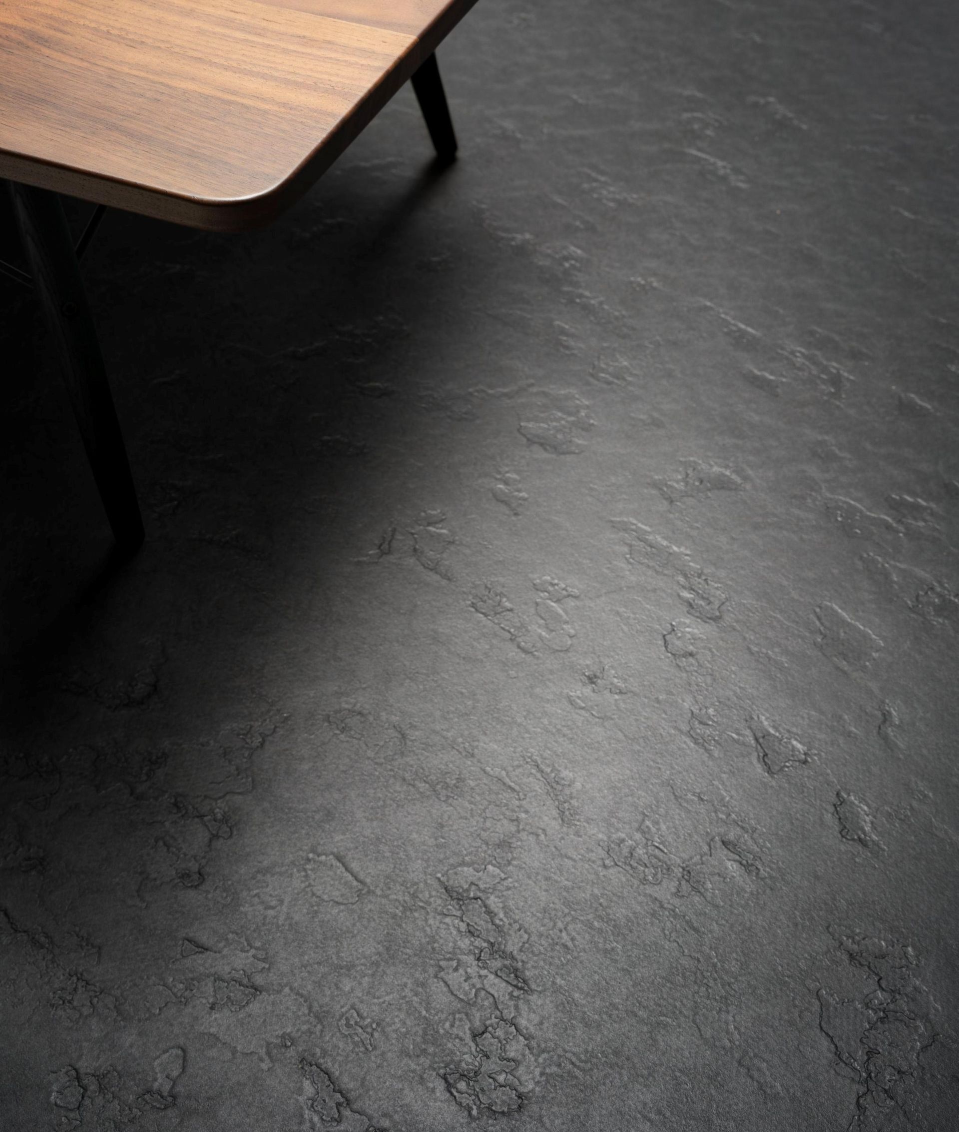 Ein Holztisch steht auf einem schwarzen Boden neben einem schwarzen Tisch.