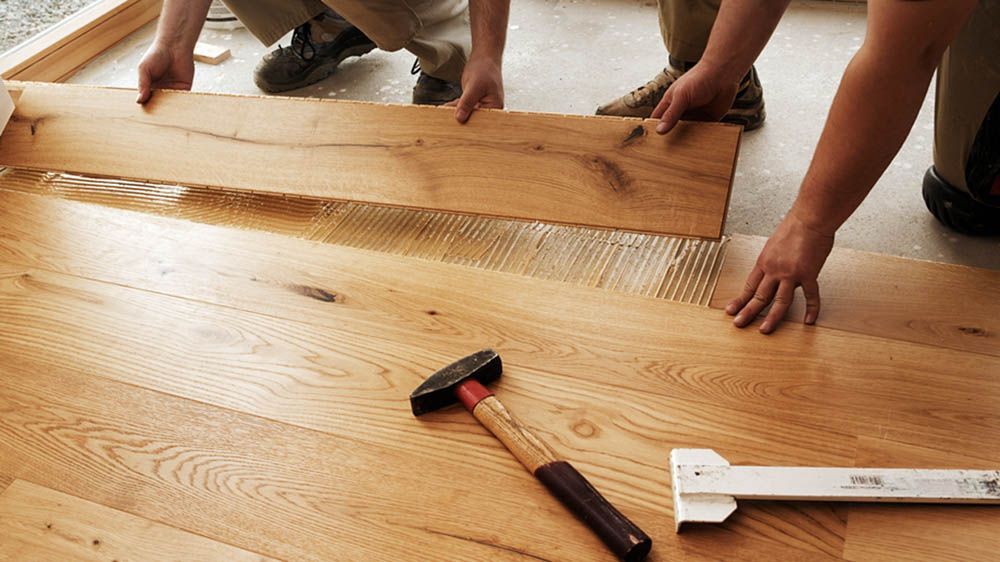 Zwei Personen verlegen einen Holzboden mit Hammer und Lineal.