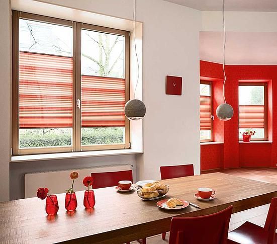 Ein Esszimmer mit Tisch und Stühlen und einem Fenster mit roten Jalousien.