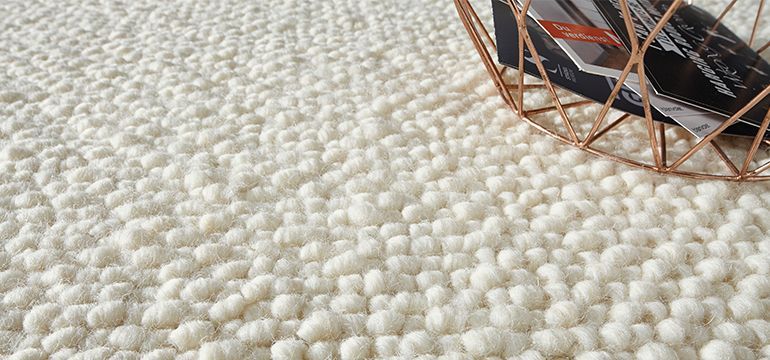 Auf einem weißen Teppich steht ein Korb mit Schuhen.