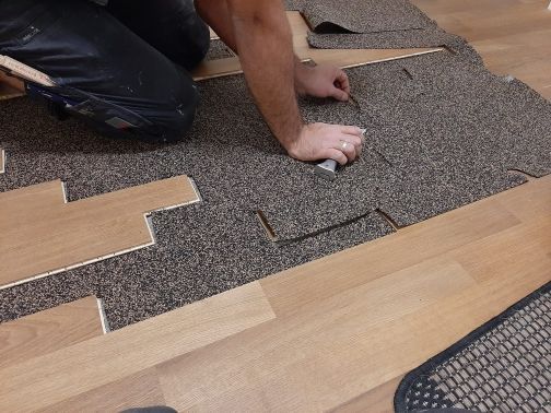 Ein Mann verlegt einen Teppich auf einem Holzboden.