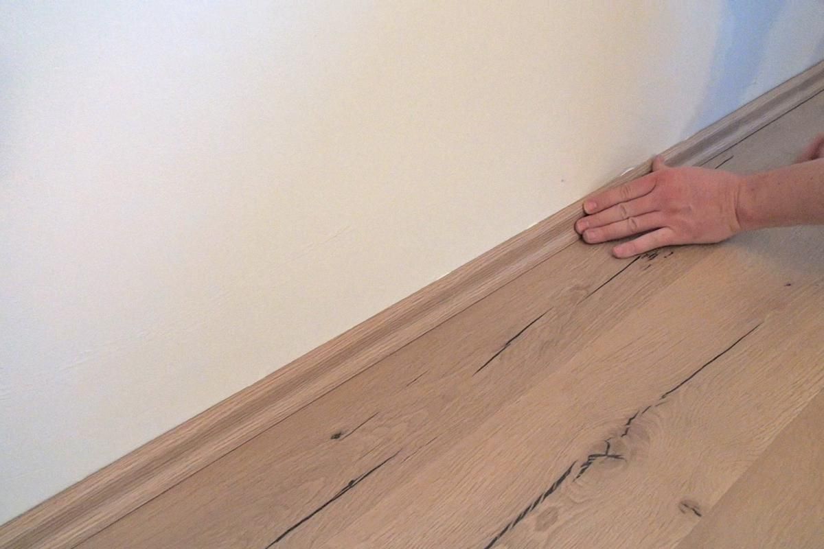 Eine Person berührt einen Holzboden neben einer Wand.