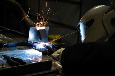 Une personne soude du métal dans un atelier sombre, des étincelles vives jaillissant.