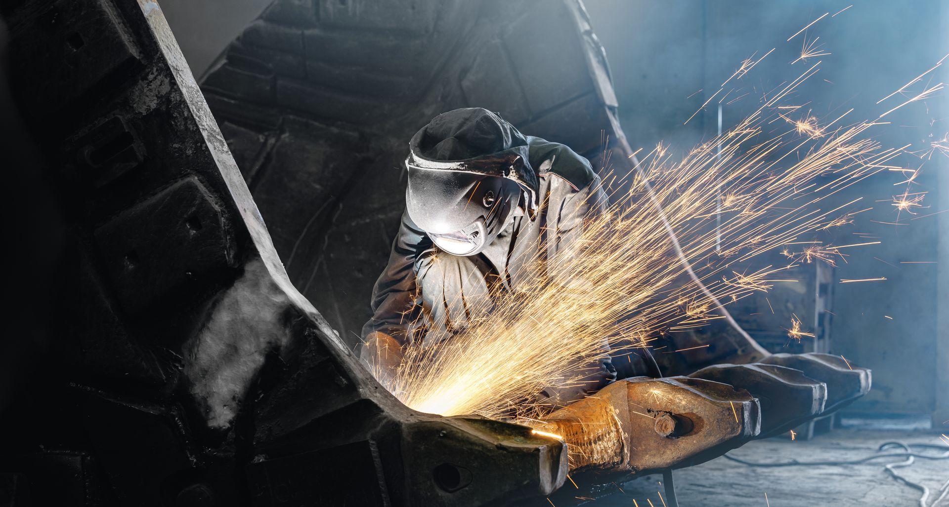Un ouvrier soude du métal dans un atelier industriel faiblement éclairé.