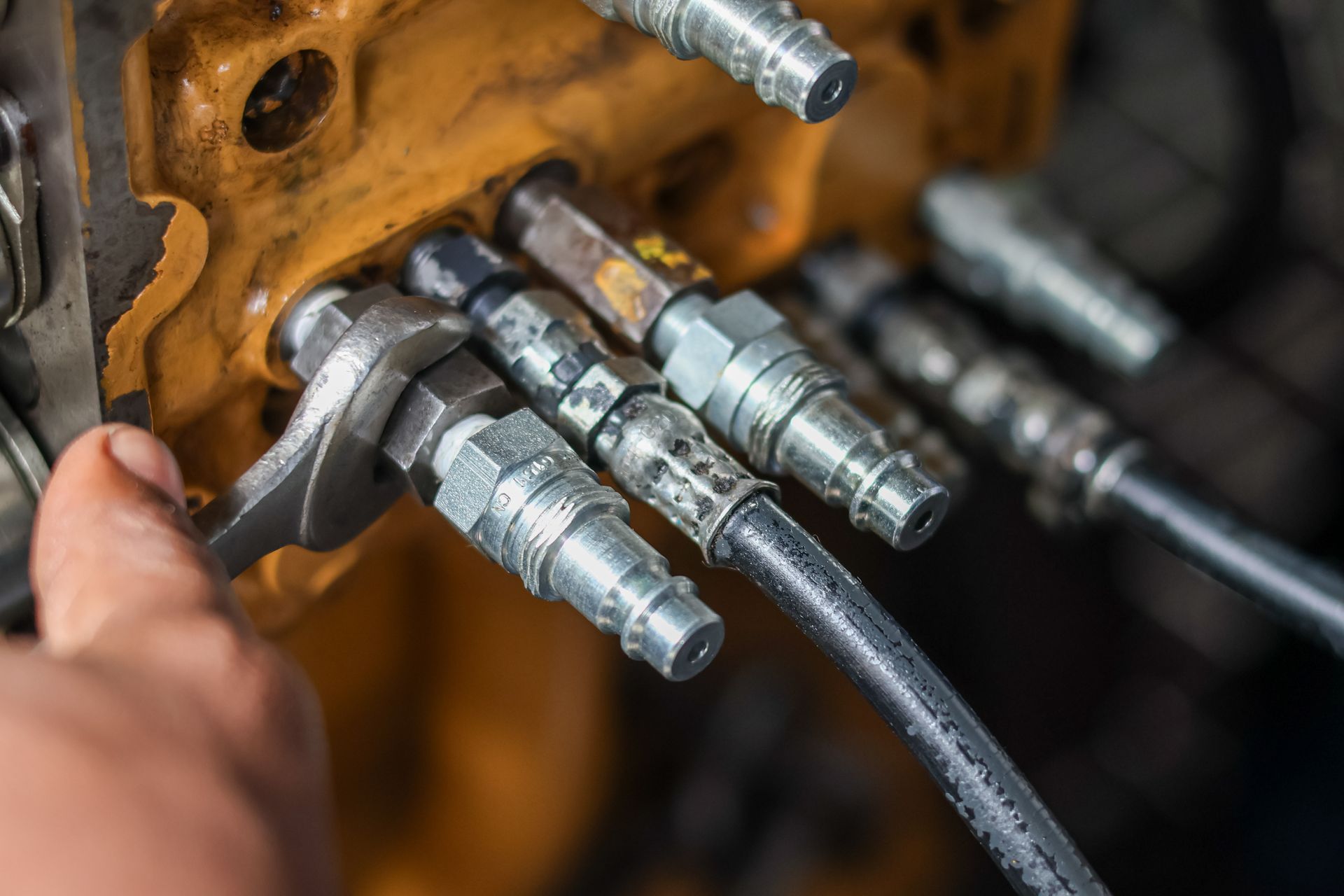 Raccordement manuel de flexibles hydrauliques à une pièce métallique jaune de machine dans un atelier