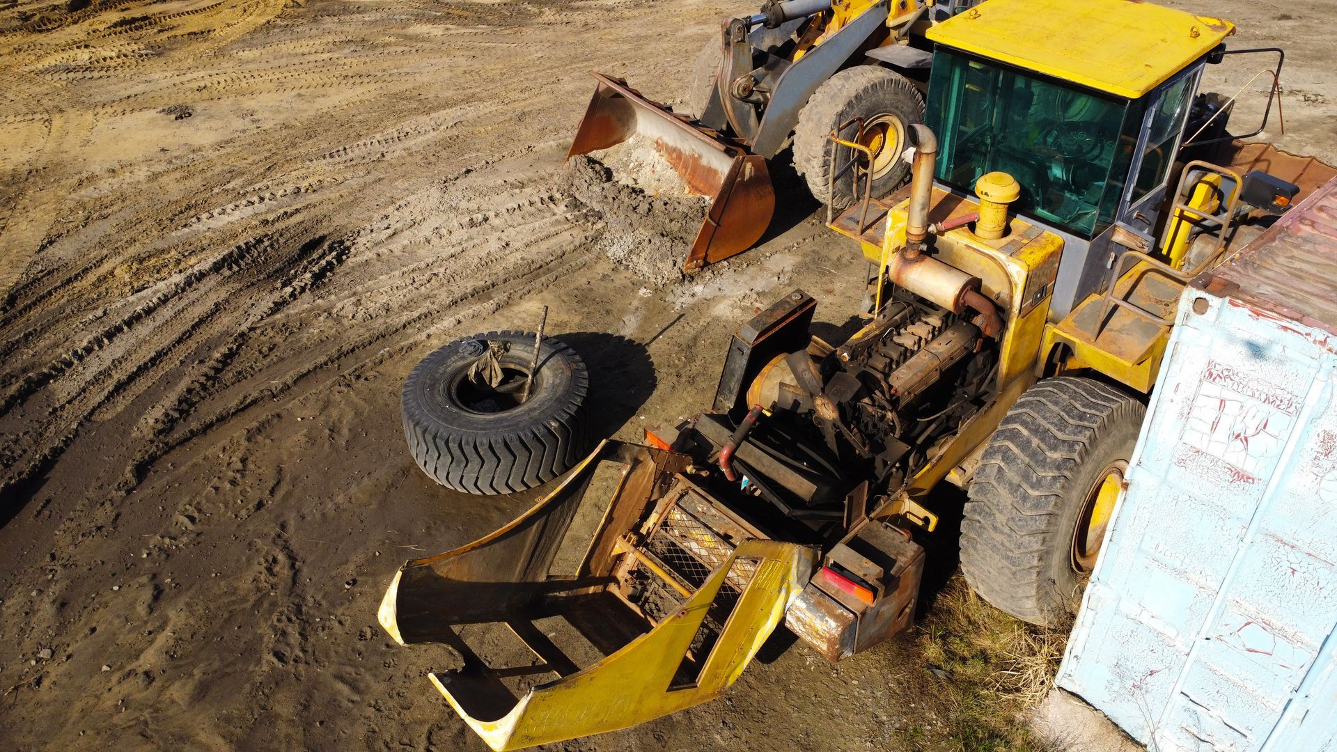 Un tracteur jaune est stationné sur de la terre avec le capot ouvert.