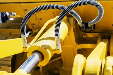 Machine hydraulique jaune avec piston brillant et tuyaux enroulés.