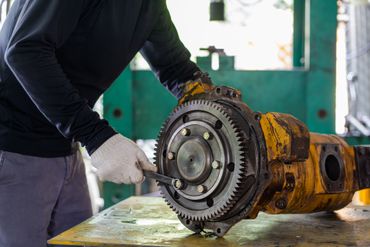 Un ouvrier ganté répare un gros engrenage jaune de machine industrielle dans un atelier.