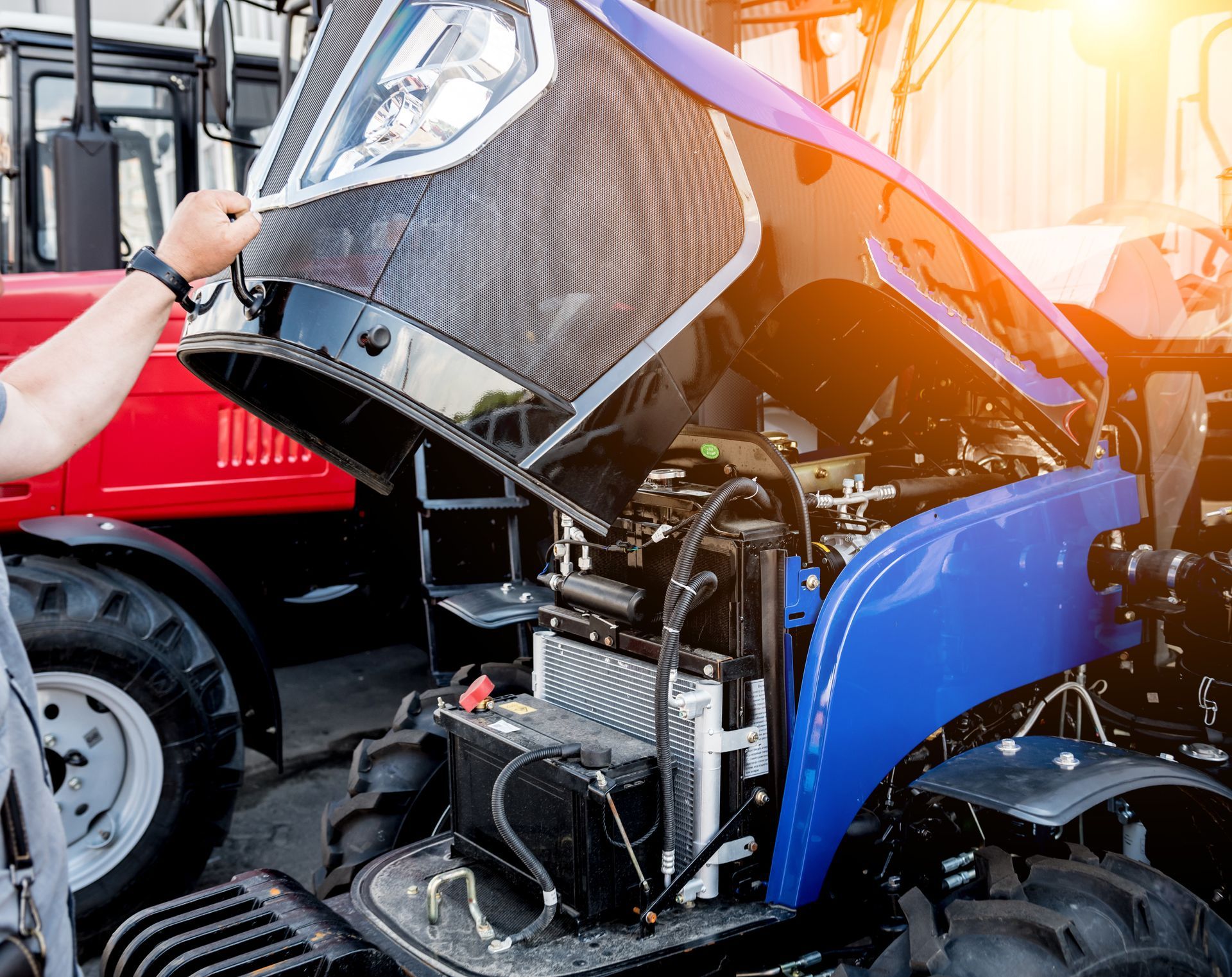 Tracteur bleu endommagé, capot ouvert, laissant apparaître des pièces du moteur.