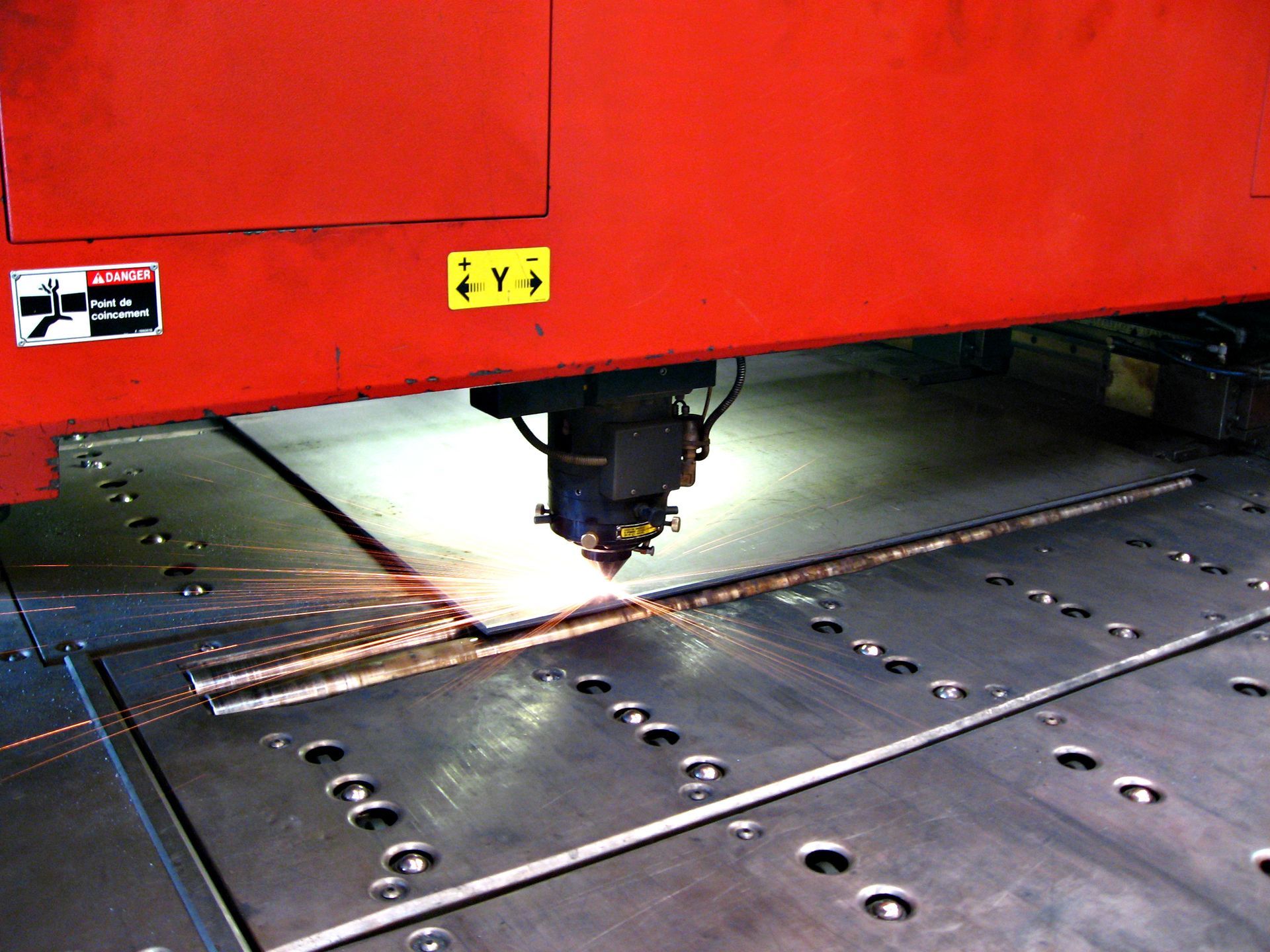 Machine de découpe laser industrielle rouge découpant une tôle de métal.