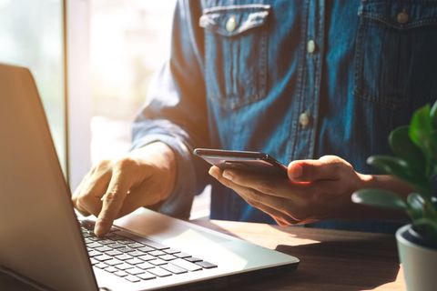 Une personne utilise un ordinateur portable tout en tenant un smartphone à un bureau.