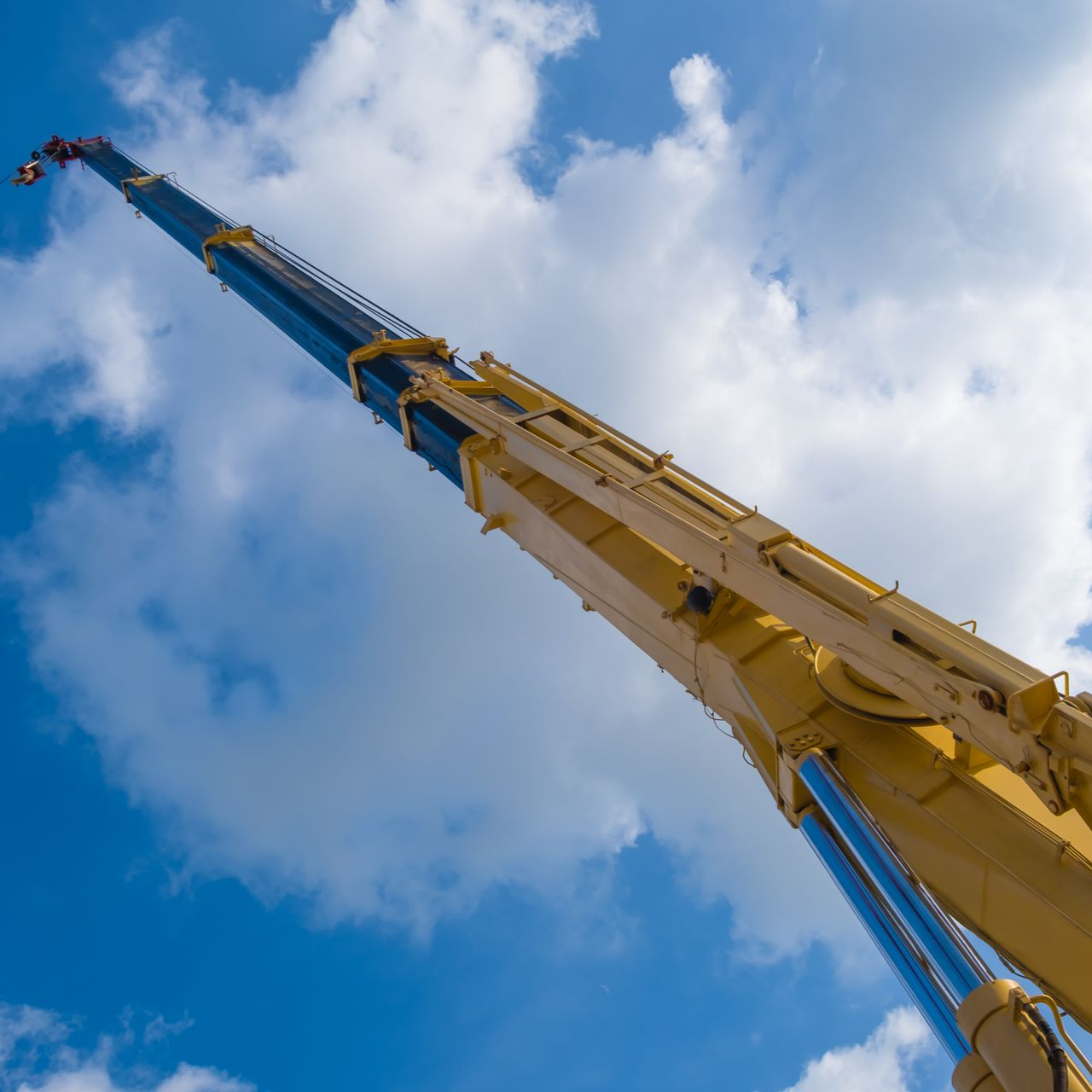 Le bras jaune d'une grue s'étend vers un ciel bleu nuageux