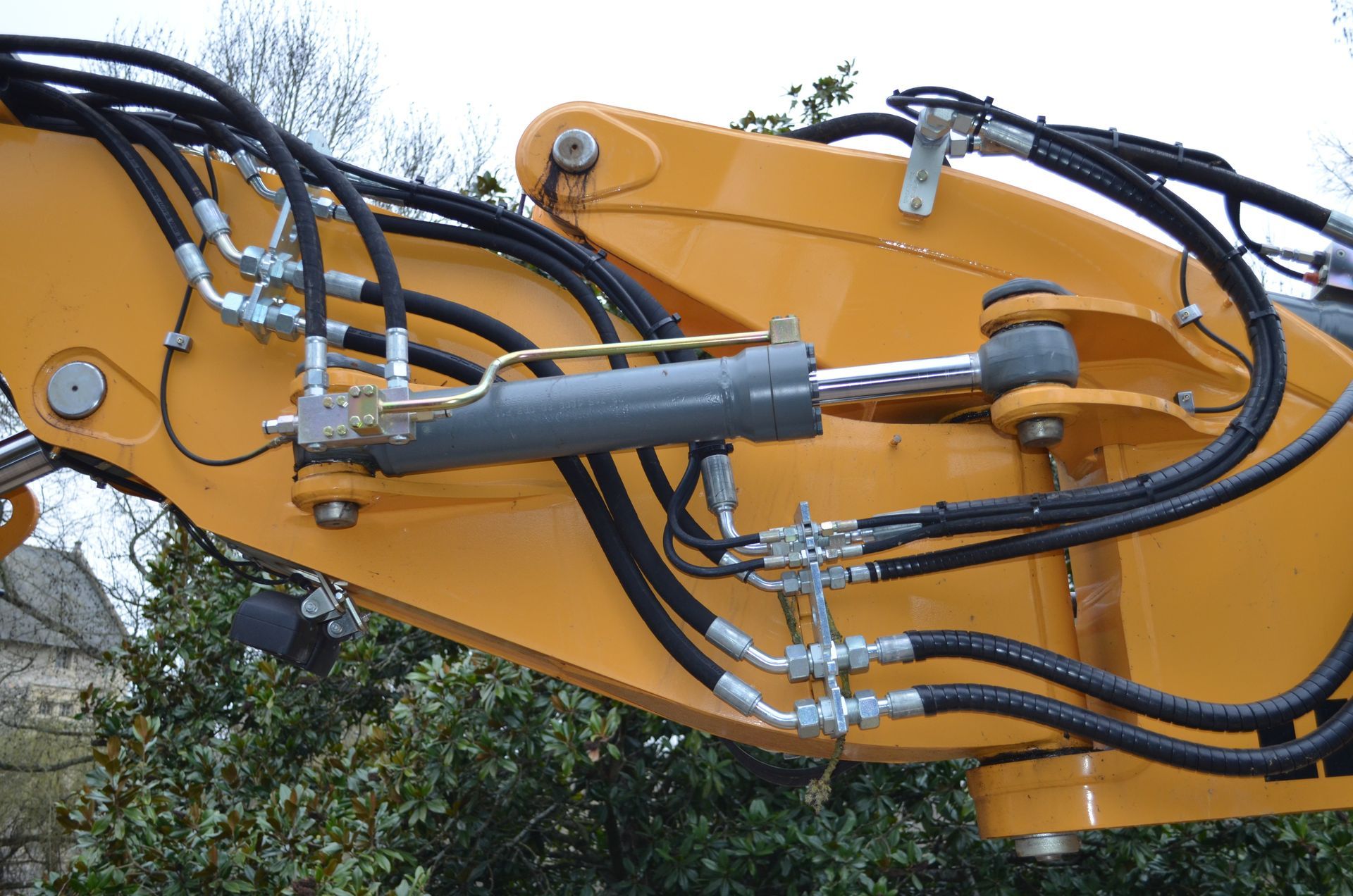 Un bras d'excavatrice jaune avec flexibles hydrauliques et vérin.