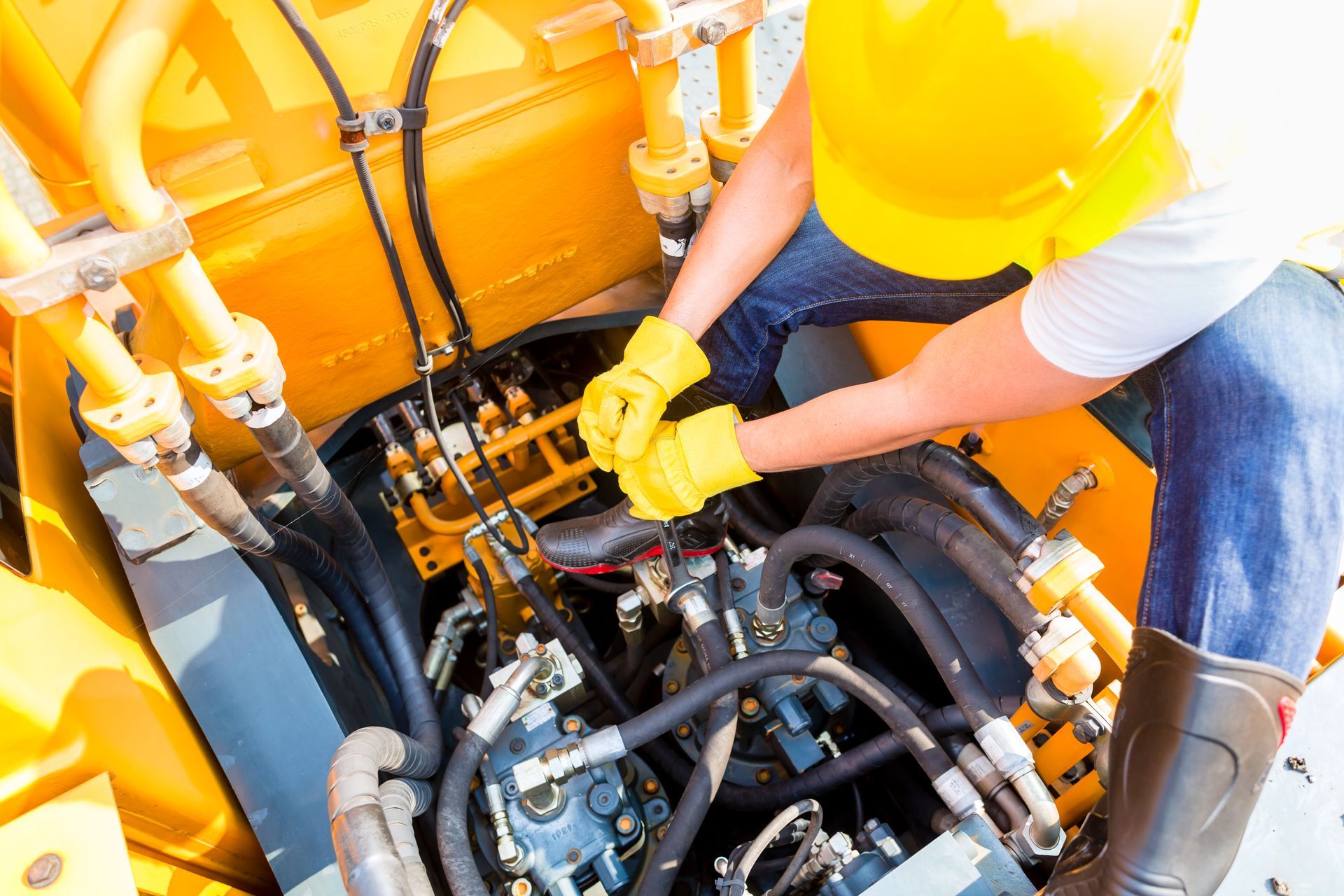 Un ouvrier portant un casque et des gants jaunes répare l'intérieur d'un tracteur.