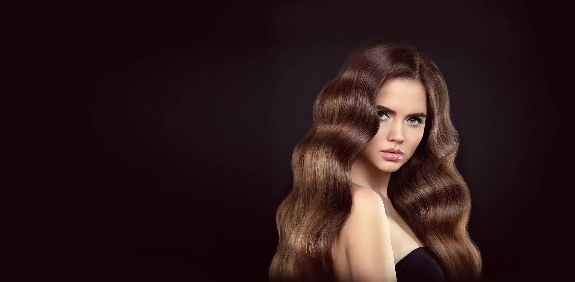 Una mujer con cabello largo y castaño lleva un top negro sin tirantes.