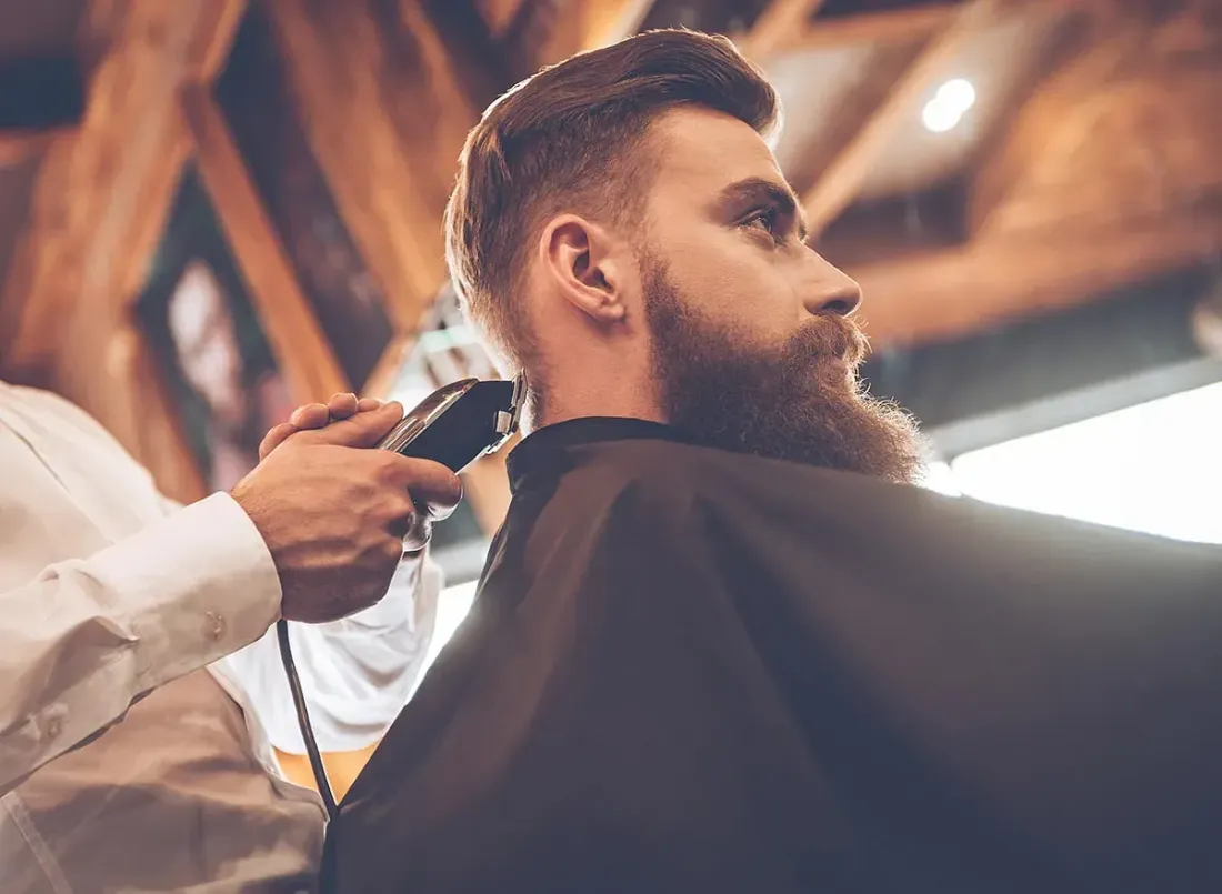 Un hombre con barba se deja cortar el pelo por un barbero.