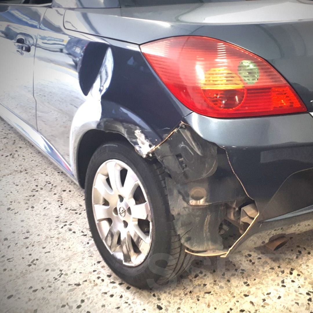 Un coche con un guardabarros dañado está estacionado en un suelo de baldosas.