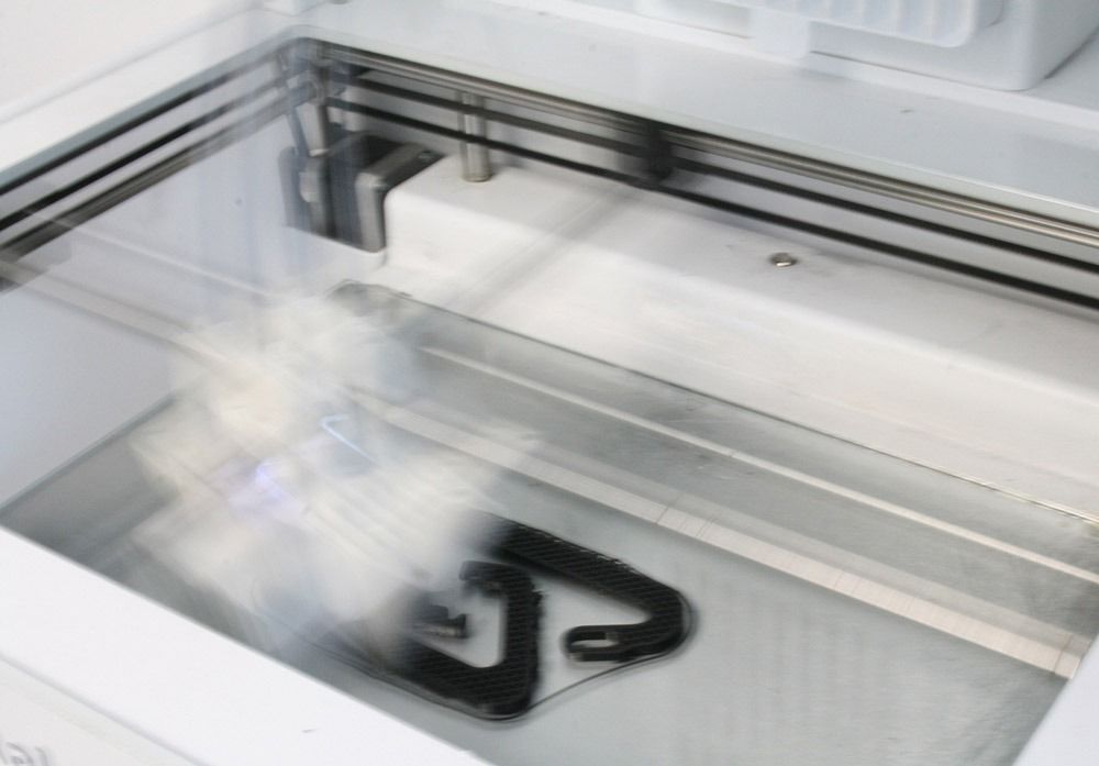 Una impresora 3D está imprimiendo un objeto negro con la letra a en él.