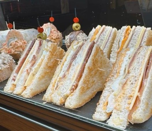 Sándwich en un plato blanco, con huevo, pimiento rojo y carne, unidos con un palillo.