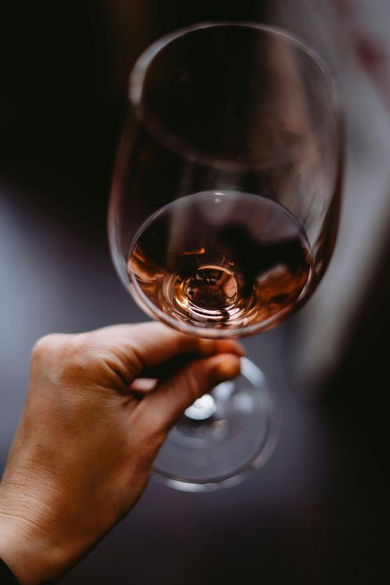 Mano sosteniendo una copa de vino llena de vino rosado, primer plano.