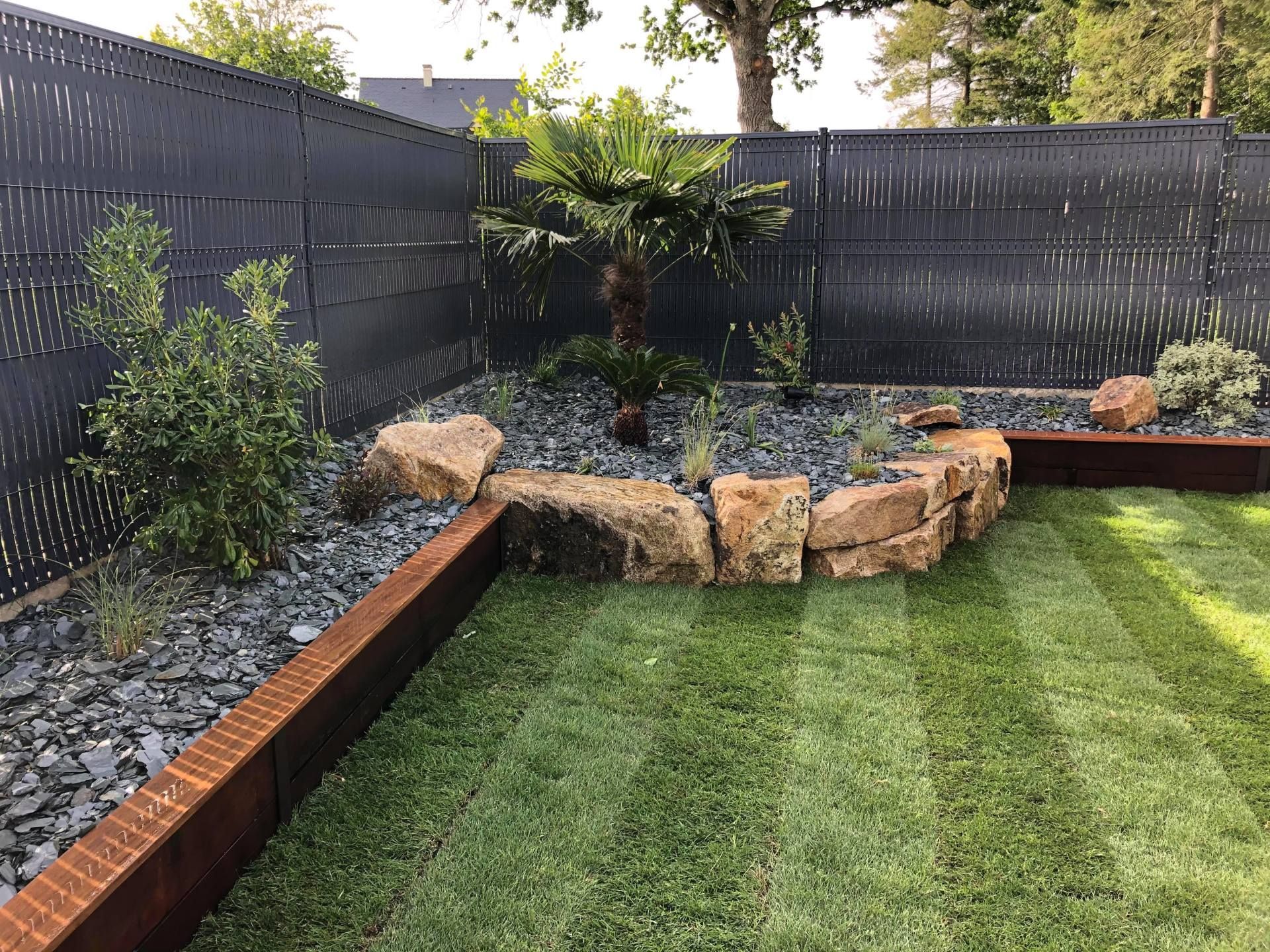 Jardin arrière avec pelouse rayée, jardinière en pierre et clôture sombre assurant l'intimité.