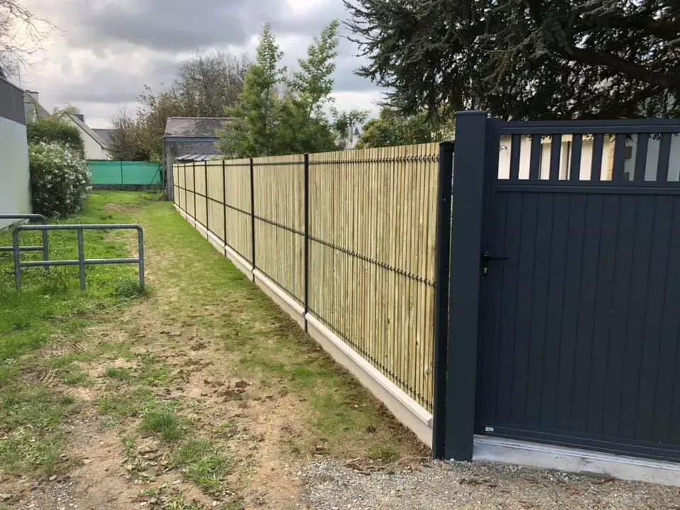 Clôture en bois avec portail bleu foncé le long d'une cour herbeuse sous un ciel nuageux.