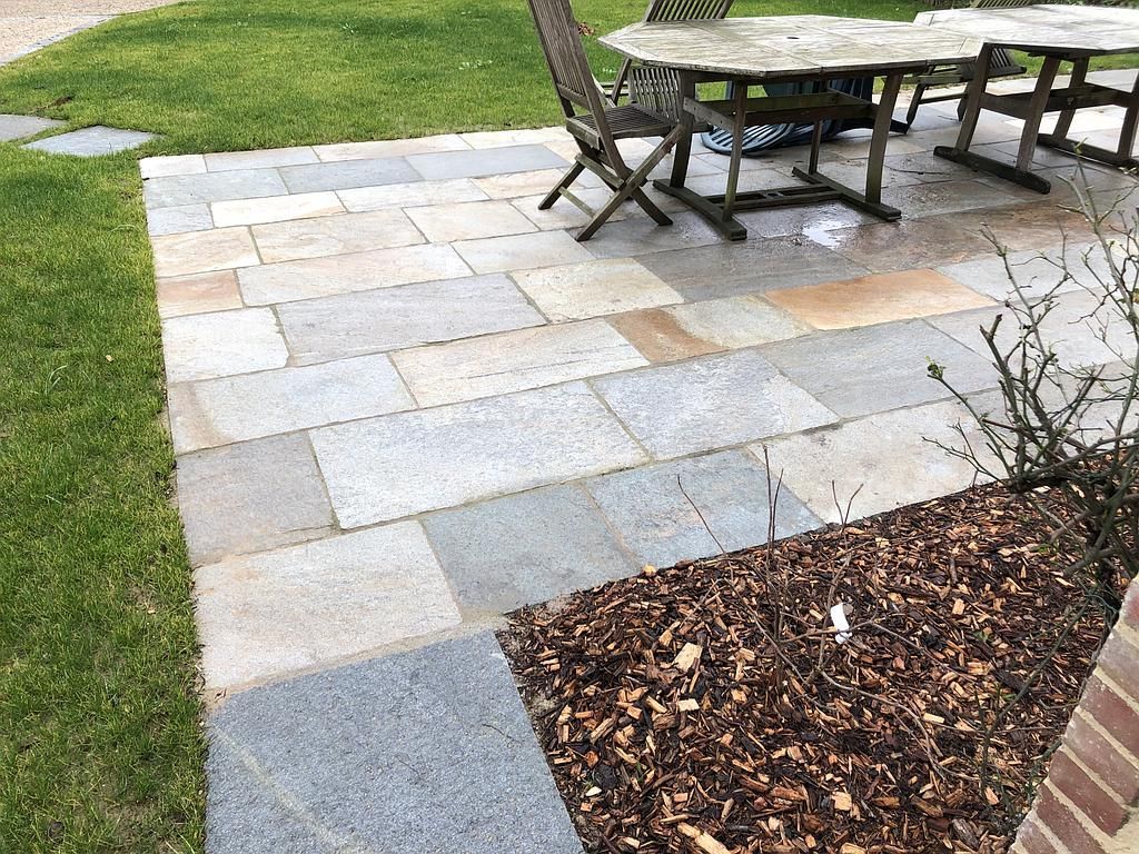 Terrasse en pierre avec table et chaises d'extérieur à côté d'une pelouse et d'un parterre de paillis.