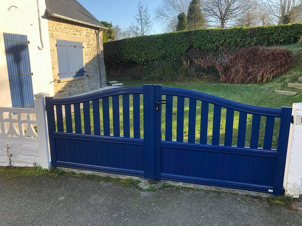 Portail d'allée en bois bleu à côté d'une maison en pierre et d'une cour gazonnée.