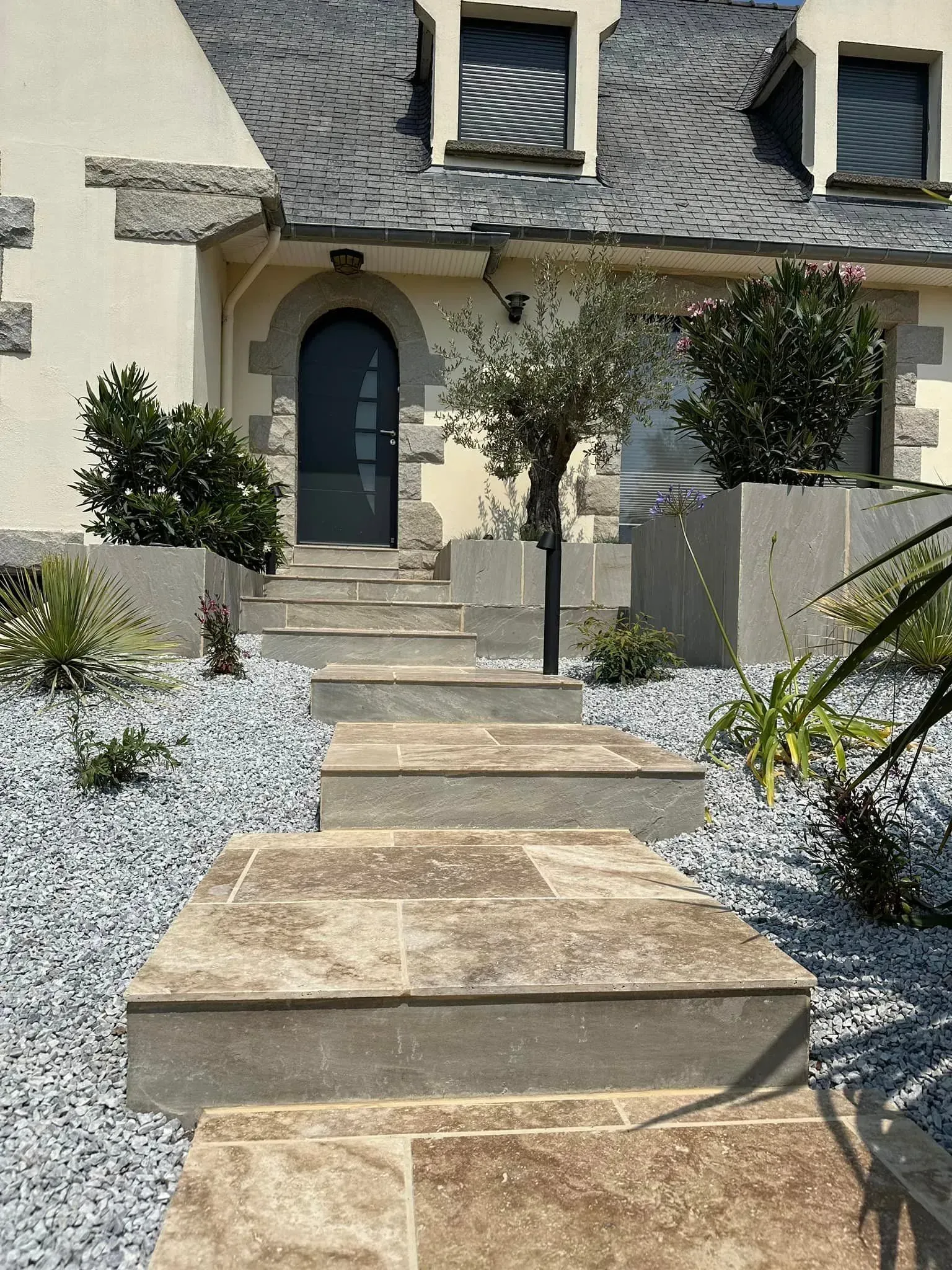 Des marches en pierre mènent à l'entrée d'une maison avec une porte bleue cintrée et un aménagement paysager désertique.